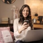 woman-sitting-on-sofa-while-looking-at-phone-with-laptop-on-920382 (1)